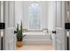 Bright bathroom showcasing a large tub beneath an arched stained-glass window, flanked by an open doorway and plant at 9985 High Falls Pointe, Johns Creek, GA 30022