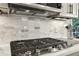 Close-up view of gas cooktop with stainless steel hood and subway tile backsplash at 1870 Marcia Overlook Dr, Cumming, GA 30041