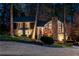 Evening view of a home featuring a stone chimney, elegant lighting and landscaped front yard at 11630 Mountain Laurel Dr, Roswell, GA 30075