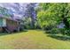 Grassy backyard with mature trees and the exterior view of the brick and vinyl home at 1956 Joseph Ct, Decatur, GA 30032