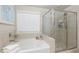 Corner bathtub and glass-enclosed shower in a bathroom with neutral tones and a large window for natural light at 211 Orchard Trl, Canton, GA 30115