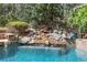 Close-up of a natural stone waterfall feature flowing into a backyard pool with lush landscaping at 3835 Paces Ferry Nw Rd, Atlanta, GA 30327