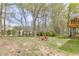 Spacious backyard featuring green grass, trees, firepit with red chairs and side view of house with wooden deck at 1545 Smoke Hill Dr, Hoschton, GA 30548