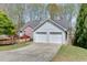 View of the home's two-car garage, brick facade, and lovely, mature trees in the front yard at 1545 Smoke Hill Dr, Hoschton, GA 30548
