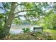 A tranquil bench sits under a tree with a scenic view of the lake, perfect for relaxation and enjoying nature at 131 Cypress St, Roswell, GA 30075