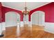 Open dining room with red accent walls, archways, hardwood floors, and a decorative chandelier at 4847 Sara Creek Way, Sugar Hill, GA 30518