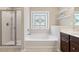 Bright bathroom features decorative window over tub, white shelves, and glass enclosed shower at 6160 Shiloh Woods Dr, Cumming, GA 30040