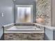 Close-up of soaking tub with stone surround and frosted window for natural light at 1007 Springharbor Walk, Woodstock, GA 30188