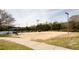 A sand volleyball court with lights and surrounding trees sits next to a sidewalk and across from the tennis courts at 4520 Vanadium Bnd, Cumming, GA 30040