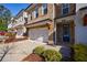 Lovely brick townhome featuring a two-car garage, well-manicured bushes, and a covered entryway at 5010 Towneship Creek Rd, Roswell, GA 30075