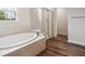 Bright bathroom with a soaking tub, glass shower, and wood-style floors at 156 Marchmont Dr, Locust Grove, GA 30248