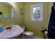 Green bathroom with oval mirror, toilet, white sink, and natural light from window at 3420 Sweetbriar Ln, Powder Springs, GA 30127