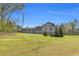 Exterior home view with sizable grass acreage, gray home and forest in background at 6585 Queen Mill Se Rd, Mableton, GA 30126
