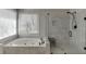 Bathroom featuring a soaking tub with window, glass shower, and grey tiled walls at 395 Highland Gate Cir, Suwanee, GA 30024