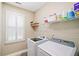 Well-lit laundry room with a window and white shelving above the washer and dryer at 6730 Waterbury Way, Cumming, GA 30040