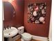 Stylish powder room featuring a round mirror, pedestal sink, toilet, and floral artwork against a deep red wall at 8070 Georgetown Cir, Suwanee, GA 30024