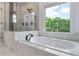 Luxurious bathroom showcasing a soaking tub with marble surround, a window, and glass enclosed shower at 5395 Lacosta Ln, Alpharetta, GA 30022