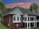 Rear view of the house showing a brick facade, covered patio, and bay windows under a colorful sunset sky at 270 Morrow Rd, Newborn, GA 30056