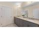 Bright bathroom with double sinks, granite countertops, grey cabinets, a large mirror, and neutral tile flooring at 4457 Equity Ct, Ellenwood, GA 30294