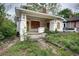 Exterior view of a distressed bungalow with boarded windows, overgrown vegetation, and a covered porch at 1366 Sylvan Sw Rd, Atlanta, GA 30310