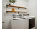 A modern laundry room with a white washer and dryer set and wood shelving for storage at 307 Downing Creek Trl, Canton, GA 30114