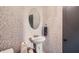 Stylish powder room featuring tiled accent wall, pedestal sink, round mirror and modern fixtures at 3011 Cravey Trl, Tucker, GA 30345