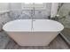 Freestanding white bathtub with chrome faucet surrounded by marble and gray tile at 9105 Old Southwick Pass, Johns Creek, GA 30022