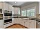 Bright kitchen features white cabinetry, stainless steel appliances, farmhouse sink and large window with wooded view at 9770 Rod Rd, Alpharetta, GA 30022