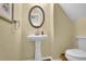 Bathroom with a pedestal sink, round mirror, toilet, and light yellow walls at 2480 Sheldon Pl, Cumming, GA 30040
