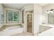Bright bathroom with a garden tub, glass shower, tile surround, and a window overlooking the yard at 9075 Preston Ln, Suwanee, GA 30024