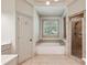Bright bathroom featuring a soaking tub, separate shower, tiled floor, and window with plantation shutters at 9075 Preston Ln, Suwanee, GA 30024