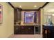 A home bar with dark wooden cabinets, tiled backsplash, a sink, beverage refrigerator, and a serving window at 440 Old Homestead Trl, Johns Creek, GA 30097