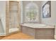 Bright bathroom features a soaking tub, shower with seat and glass door, hardwood floor, and natural light at 8385 Sentinae Chase Dr, Roswell, GA 30076