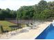 Community pool with lounge chairs, a table and tennis courts surrounded by trees at 6040 Carriage Dr, Cumming, GA 30028