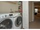 Functional laundry room with washer, dryer, shelving, and a view into the main bedroom at 310 Brittany Ct, Duluth, GA 30096