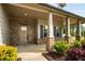 Inviting covered porch with stone accents and stately columns with a green and red manicured garden at 209 Brynn Ln, Mcdonough, GA 30252