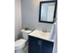 Stylish powder room features a dark vanity, a square mirror, and a white commode with green plant at 5990 Arbor Green Cir, Sugar Hill, GA 30518