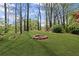 A stone fire pit surrounded by a lush green lawn and mature trees in a serene backyard setting at 135 Ardsley Run, Canton, GA 30115
