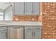 Corner view of modern gray kitchen cabinets and stainless steel appliances with a brick accent wall at 3229 Summer Stream Nw Ln, Kennesaw, GA 30152