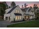 Exterior view of a modern farmhouse, featuring black frame windows, and a lush green lawn at twilight at 120 Farm Gate Dr, Woodstock, GA 30188