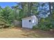 A white storage shed is nestled in a backyard with lush greenery and a wooded backdrop at 1112 Autumn Glen Way, Dacula, GA 30019