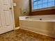 Close-up of a bathtub with tan tiles, next to a door, and a window with sunlight at 445 Pintail Ct, Suwanee, GA 30024