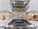 Modern kitchen featuring a stainless steel cooktop, brick backsplash, and stylish white cabinetry at 6380 Cortland Walk, Alpharetta, GA 30005