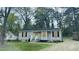 Quaint bungalow-style home with boarded windows, a concrete driveway, and verdant trees surrounding the property at 4262 Lindsey Dr, Decatur, GA 30035