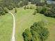 Picturesque aerial view of a vast grassy field surrounded by lush trees and a winding gravel driveway at 5187 Parkview Rd, Social Circle, GA 30025