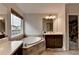 Bright bathroom featuring a soaking tub with tile surround and a vanity with wood cabinets at 4650 Sandy Creek Dr, Cumming, GA 30028