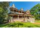 A beautiful two-story brick home with a turret and wraparound porch is surrounded by green grass and trees at 3593 Hemphill St, Atlanta, GA 30337