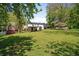 Expansive backyard with lush green lawn, mature trees, colorful flowering bushes, and a covered patio area at 313 Ellenwood Dr, Bowdon, GA 30108
