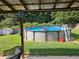 Backyard view of above ground pool with a green lawn, a shed, trees, and a covered patio at 309 Daffodil Dr, Temple, GA 30179
