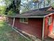 Side view of the home's exterior featuring dark red siding and dark shingle roof at 520 Pine Dr, Pine Lake, GA 30072